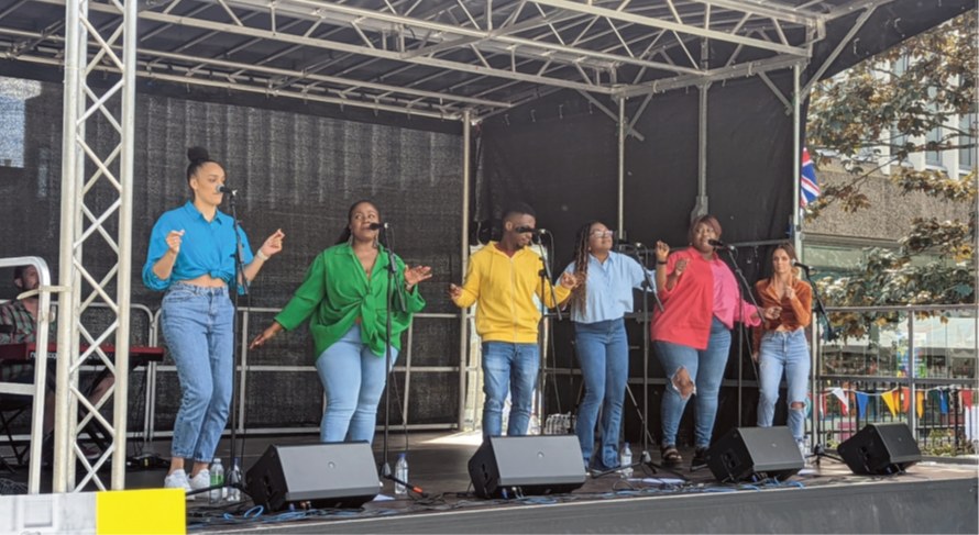 Group of six singers in colourful shirts singing and dancing on stage