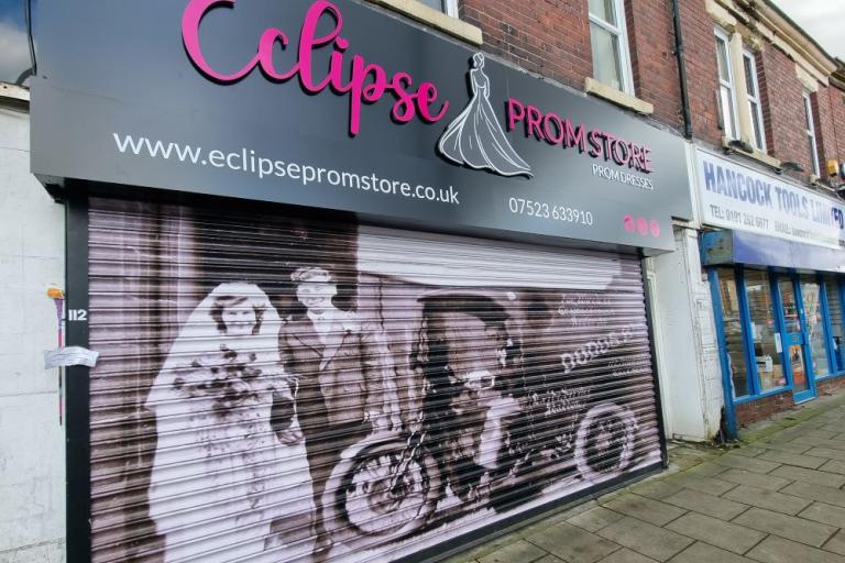 A colour photo of a prom dress shop with a vinyl of a black and white photo covering its shutters