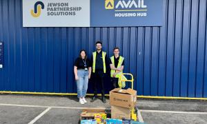 Three people standing behind a pile of gifts with signs behind them reading Jewsons and Avail Housing hub